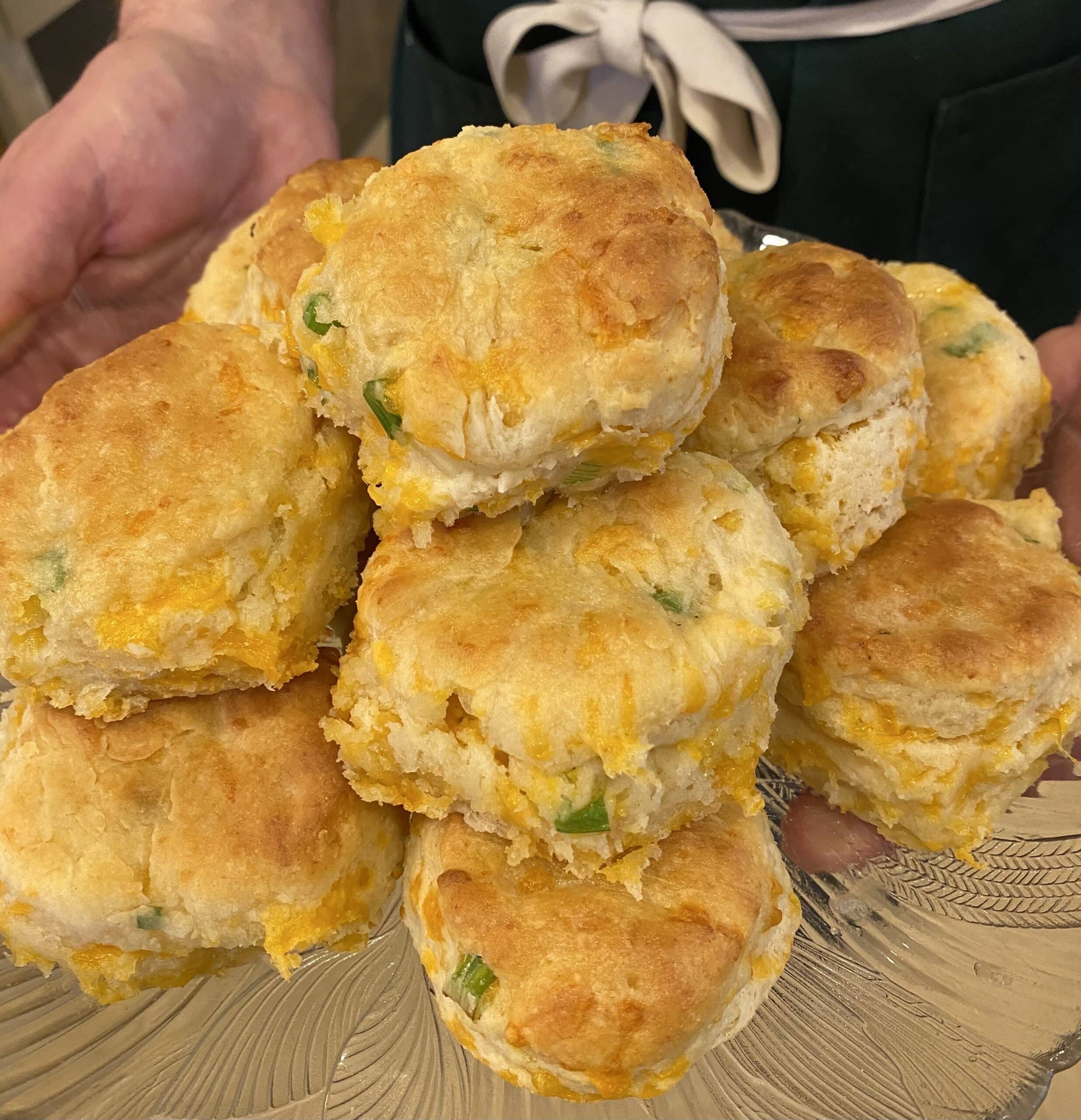 a hand holding a plate of cheddar scallion bisiuts