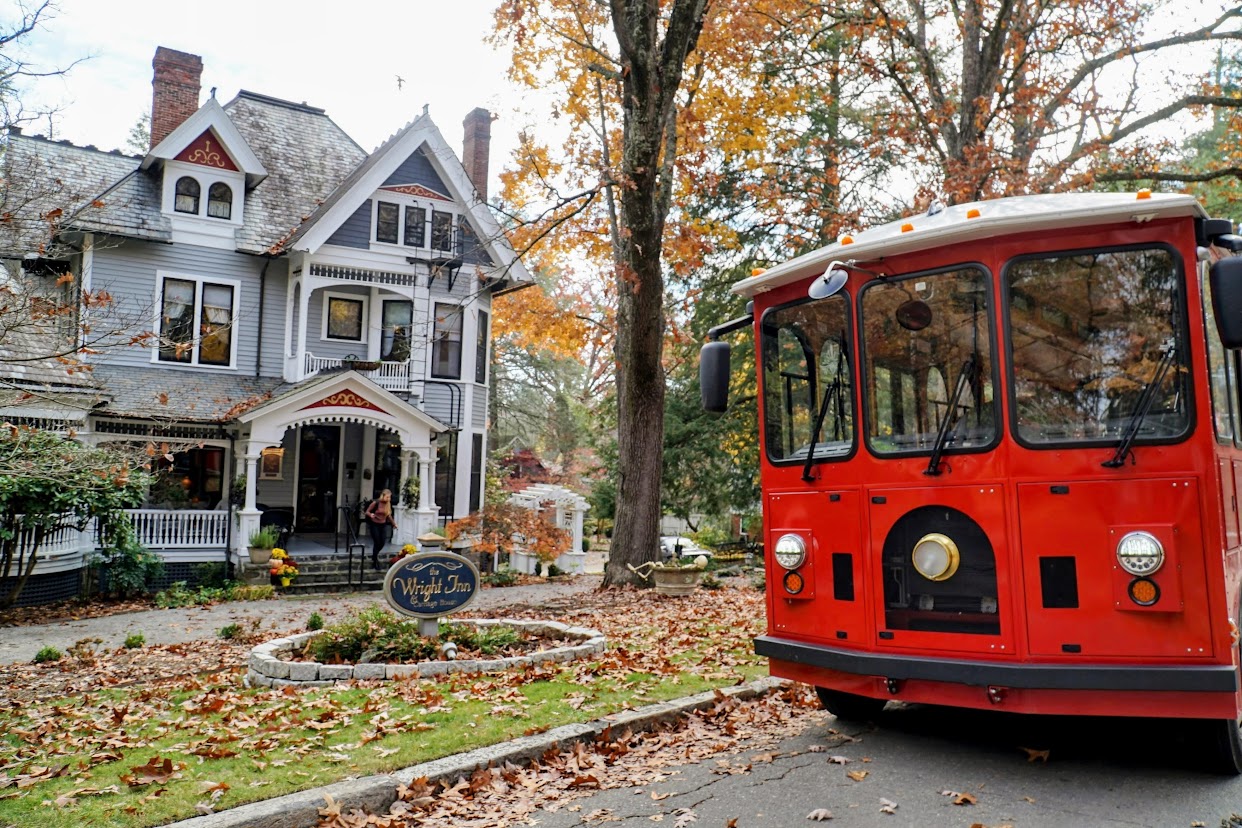 a red trolley in front of a gray Victorian house on a fall day