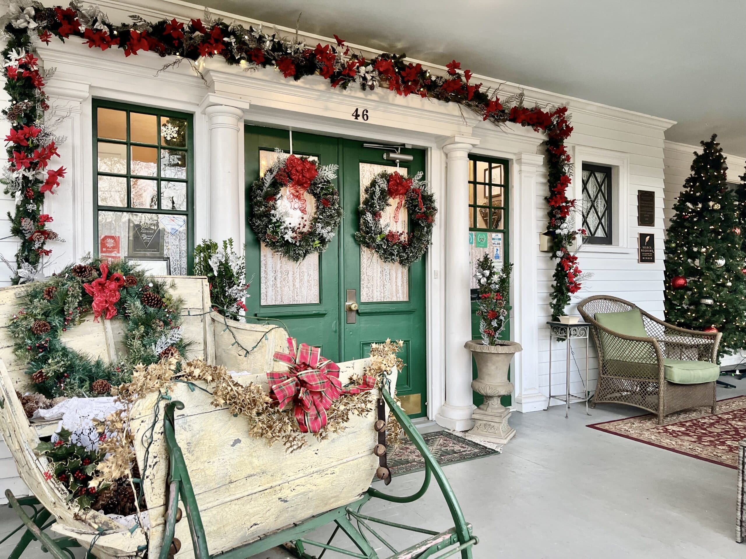 I set of doors on a porch that is decorated with garland and christmas wreaths