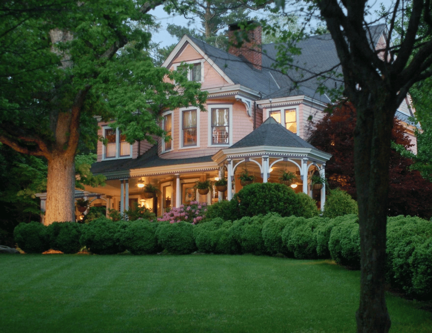 ext of pink 2 story victorian B&B with lush green hedges and a gazebo porch