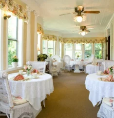 enclosed porch with wicker tables and chairs set for breakfast