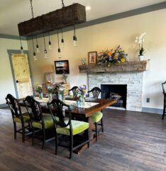 a long wooden dining room table and chairs set with dinnerware in a room with a stack stone fireplace in a B&B