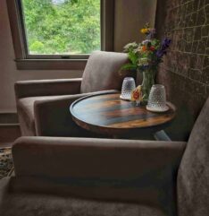 two upholstered brown chairs with a side table between them, glasses and flowers with a window view