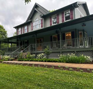 2-story gray farmhouse with burgundy shutters, wrap around porch and sidewalk to greet guests at a B&B
