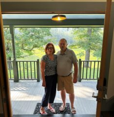 a red headed woman and brown haired man standing together on a porch who are innkeepers